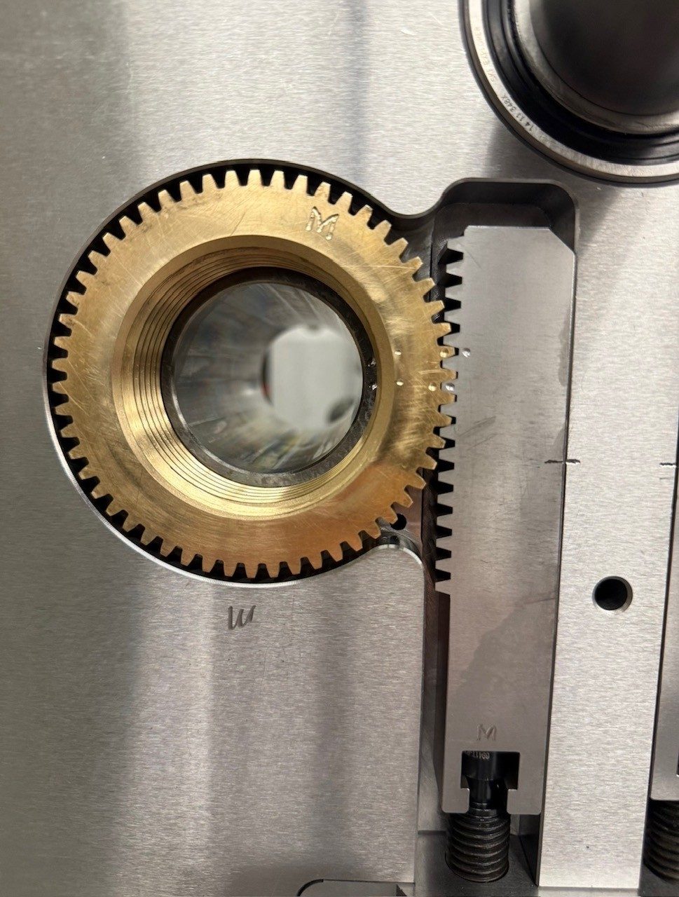 A brass gear meshed with a rack, mounted on a mold plate