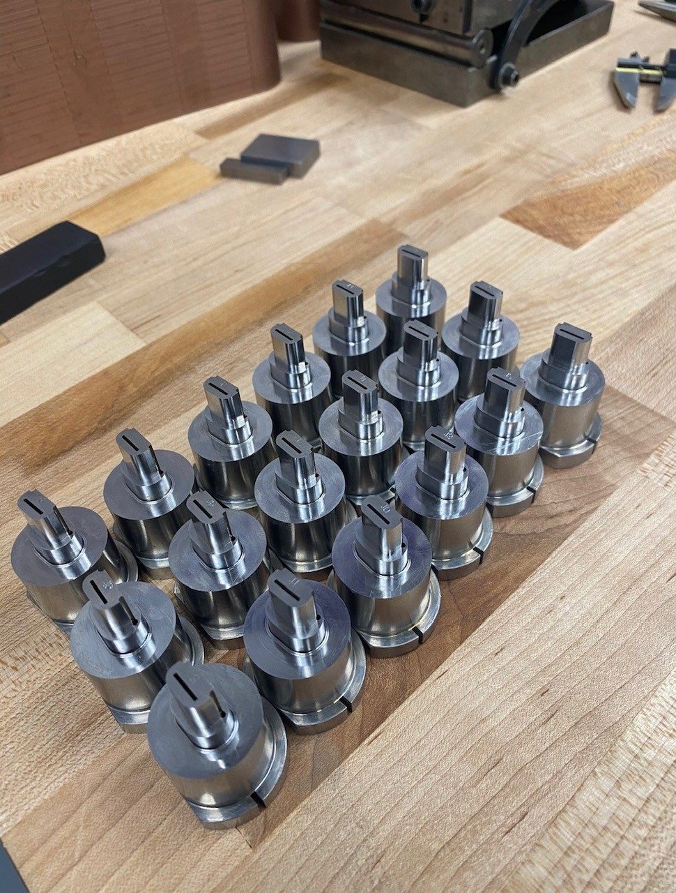 Rows of finished machined metal pins and inserts laid out on a workbench